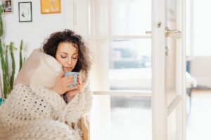 woman wrapped in blanket sipping beverage at home