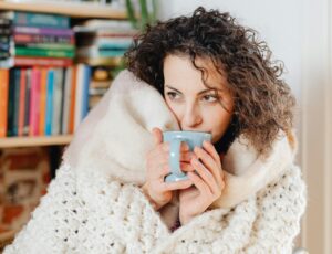 woman covered in blankets sipping beverage